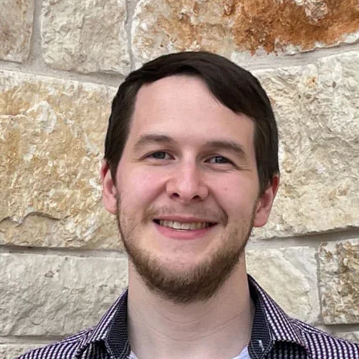 Oliver Papa-Garcia smiling in front of a textured stone wall