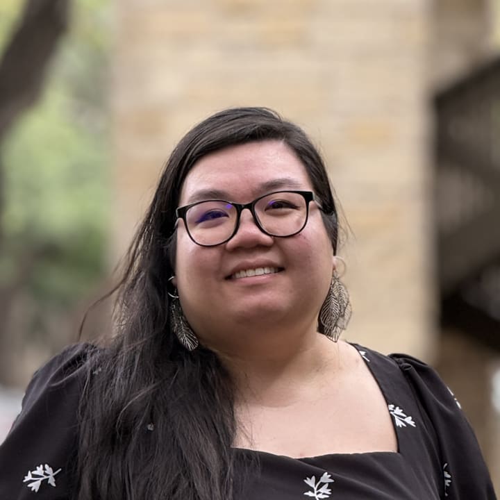 Lily Nguyen smiling outdoors in a black floral dress and round glasses
