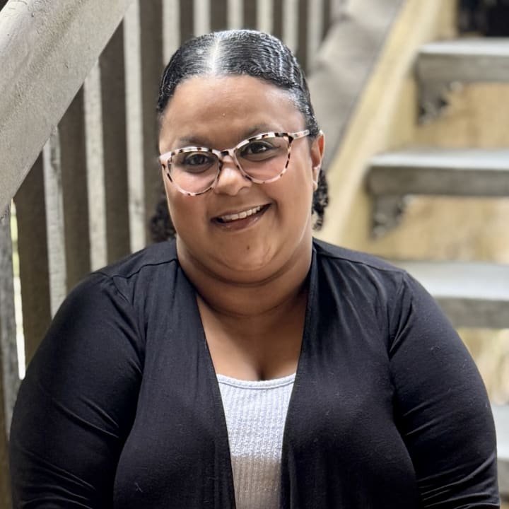 Ivana Crumpton smiling on a wooden staircase in glasses