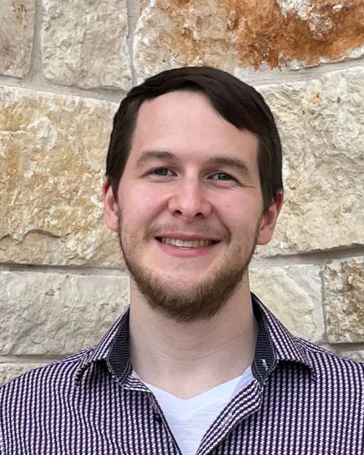 Oliver Papa-Garcia smiling in front of a textured stone wall