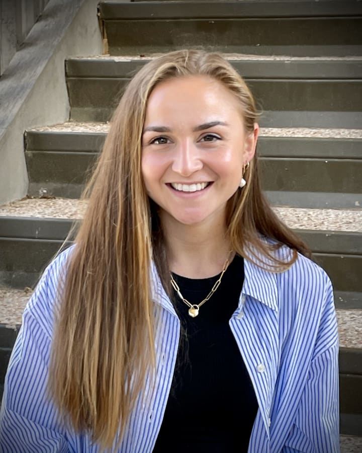 Bailey Pellissier smiling on grey steps in a striped shirt