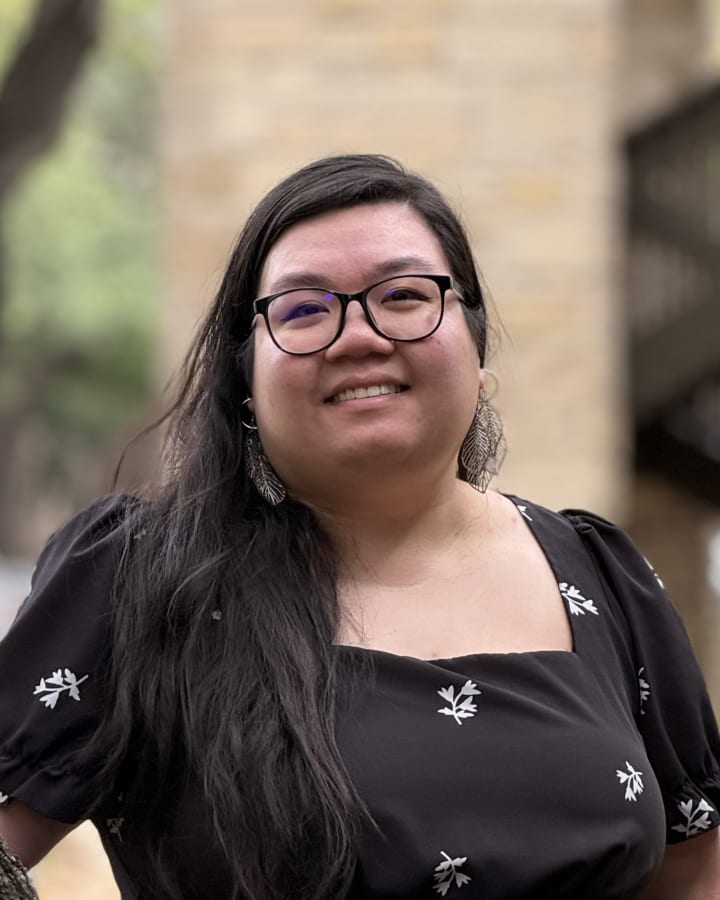 Lily Nguyen smiling outdoors in a black floral dress and round glasses