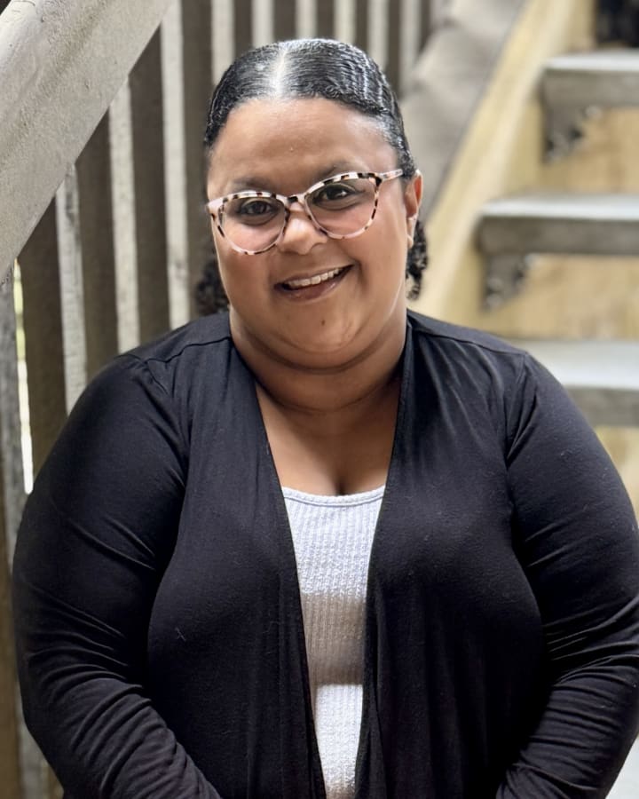 Ivana Crumpton smiling on a wooden staircase in glasses
