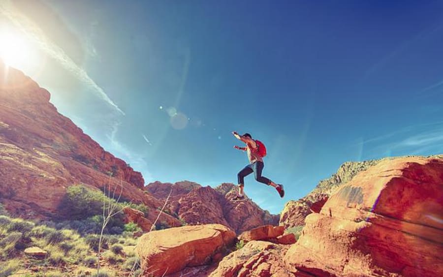 A man leaping between red rock ledges under a bright sky