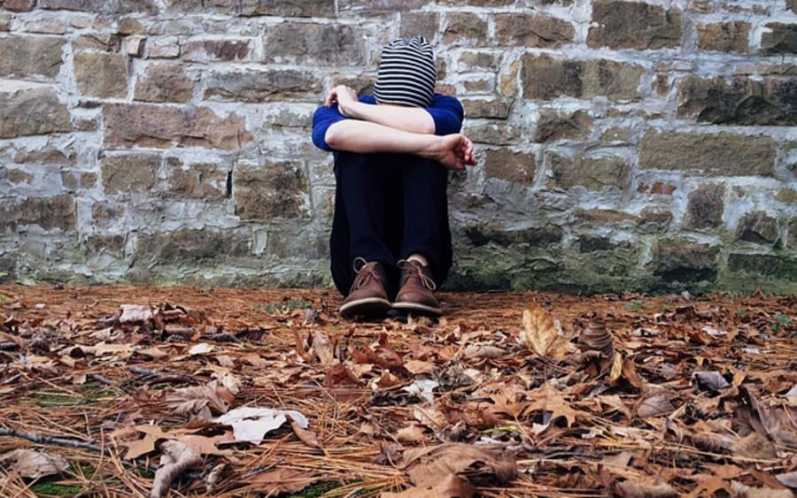 A person sitting against a stone wall among fallen leaves