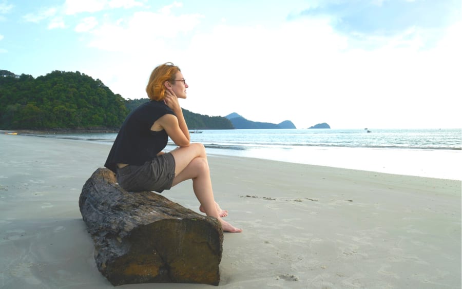 A woman sitting on a log at the beach, looking out at the water
