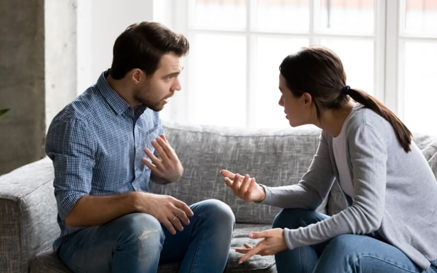 A couple mid-conversation on a grey sofa