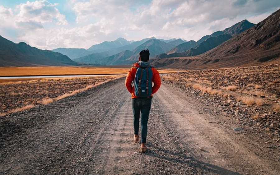 A hiker walking a dirt path toward distant mountains