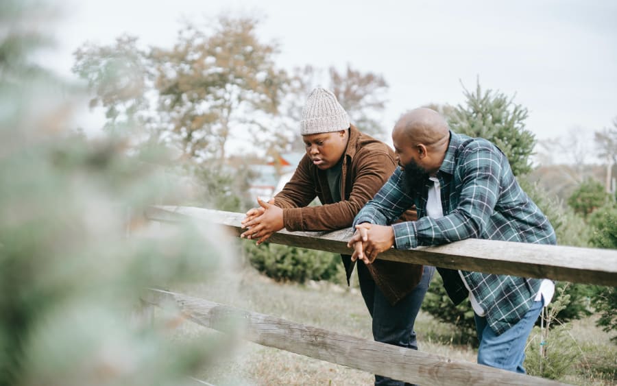 Two men leaning on a wooden fence outdoors, talking